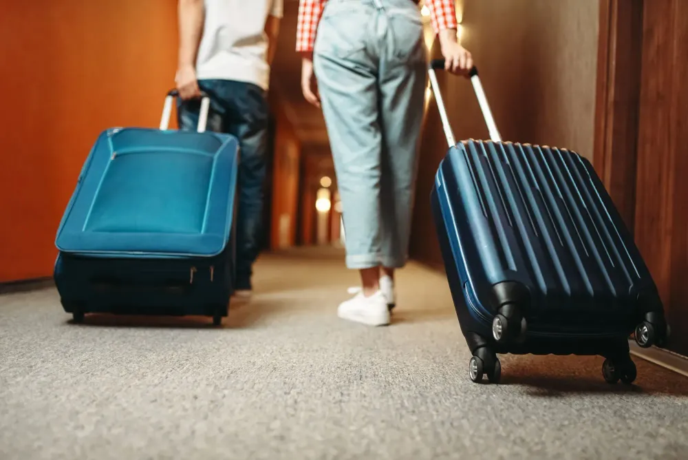 Two people wheeling rolling suitcases down a hotel hallway